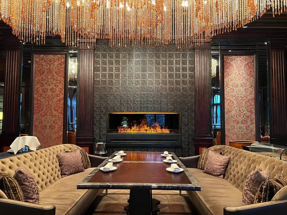 Паровой камин iVENGO в ресторане отеля Four Seasons в Петербурге: линия огня в стене с серебряной чеканкой, над ней хрустальная люстра, вокруг диваны и накрытый стол